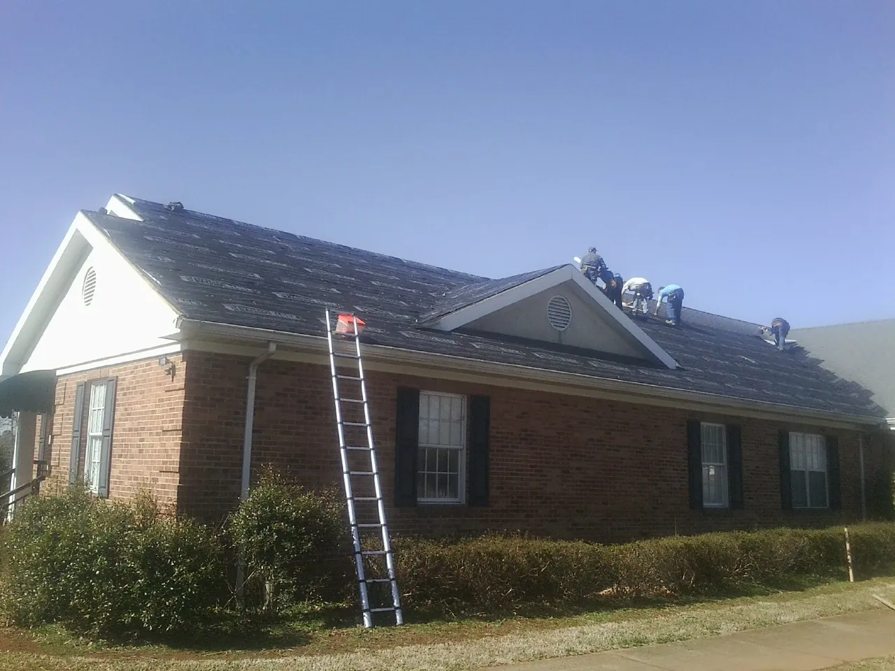 Crew tearing shingles off a brick ranch roof with a ladder set — Emergency Roof Repair work by our crew in Leeds