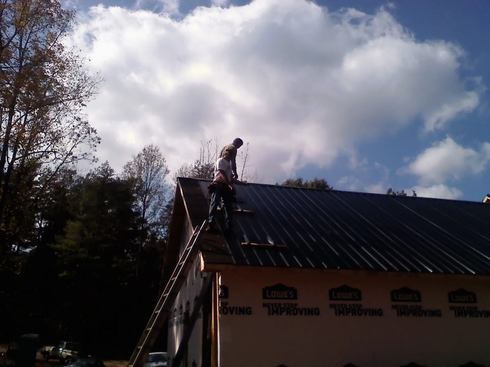 Roofer fastening dark metal panels high against a cloudy sky, from a Roof Inspection job in Leeds