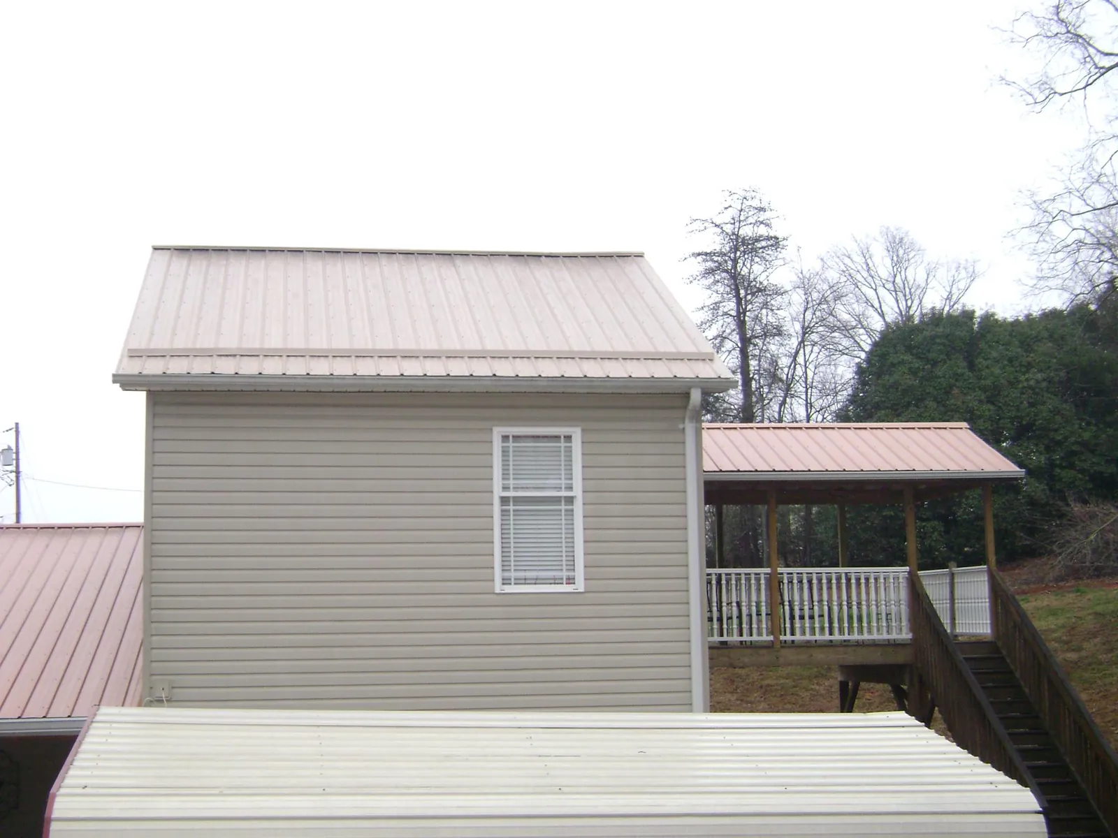 Tan metal roofs on a two story addition and attached porch, from a Roof Replacement job in Leeds